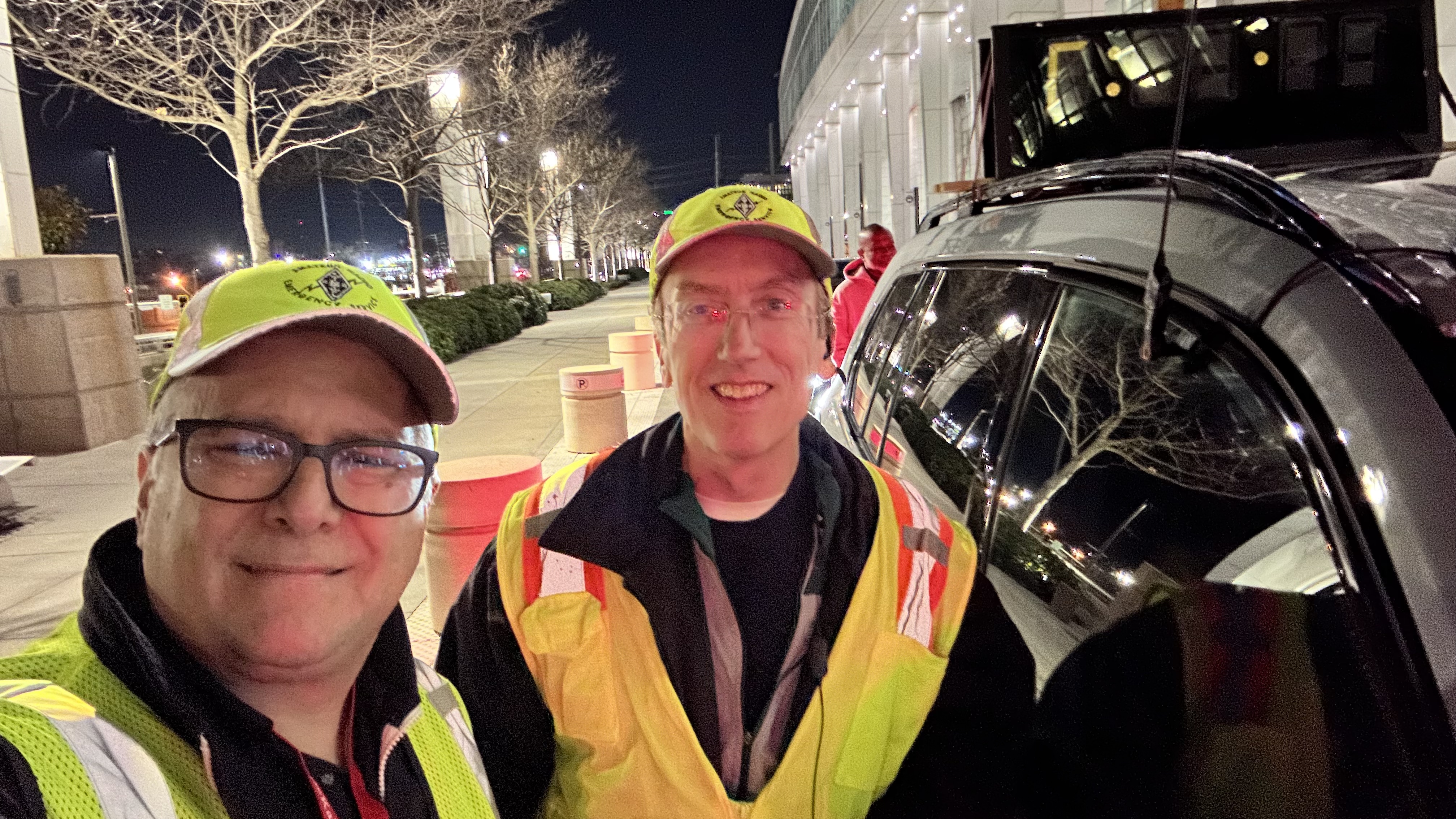 Two DKARES operators in yellow safety vests and ARES caps at the pre-dawn marathon staging area before the start of the 2026 Atlanta Marathon.