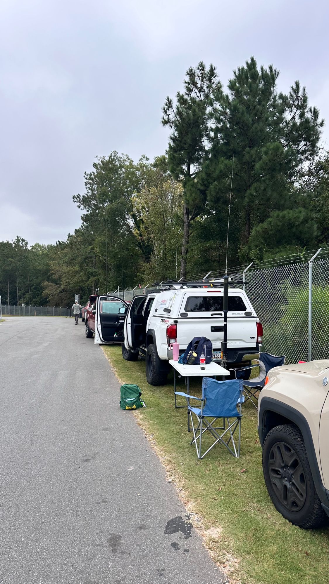 Member vehicles parked along a fence line with antennas raised, a folding table and chairs set up beside a pickup truck