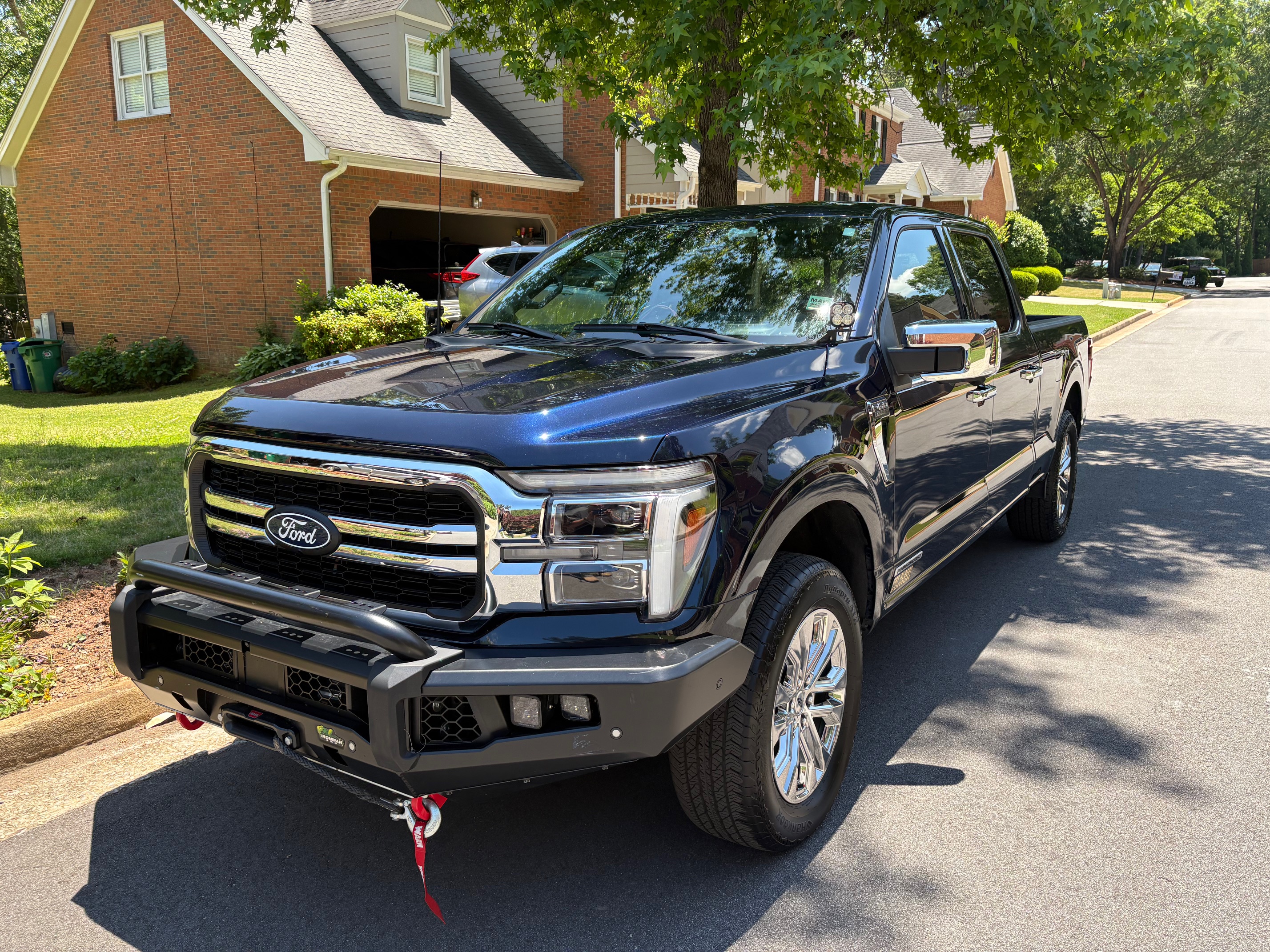 KJ4ZZB's 2024 Ford F-150 PowerBoost in dark blue, parked in a residential driveway. IronMan front bumper with winch fairlead and red recovery hook visible at the bottom.